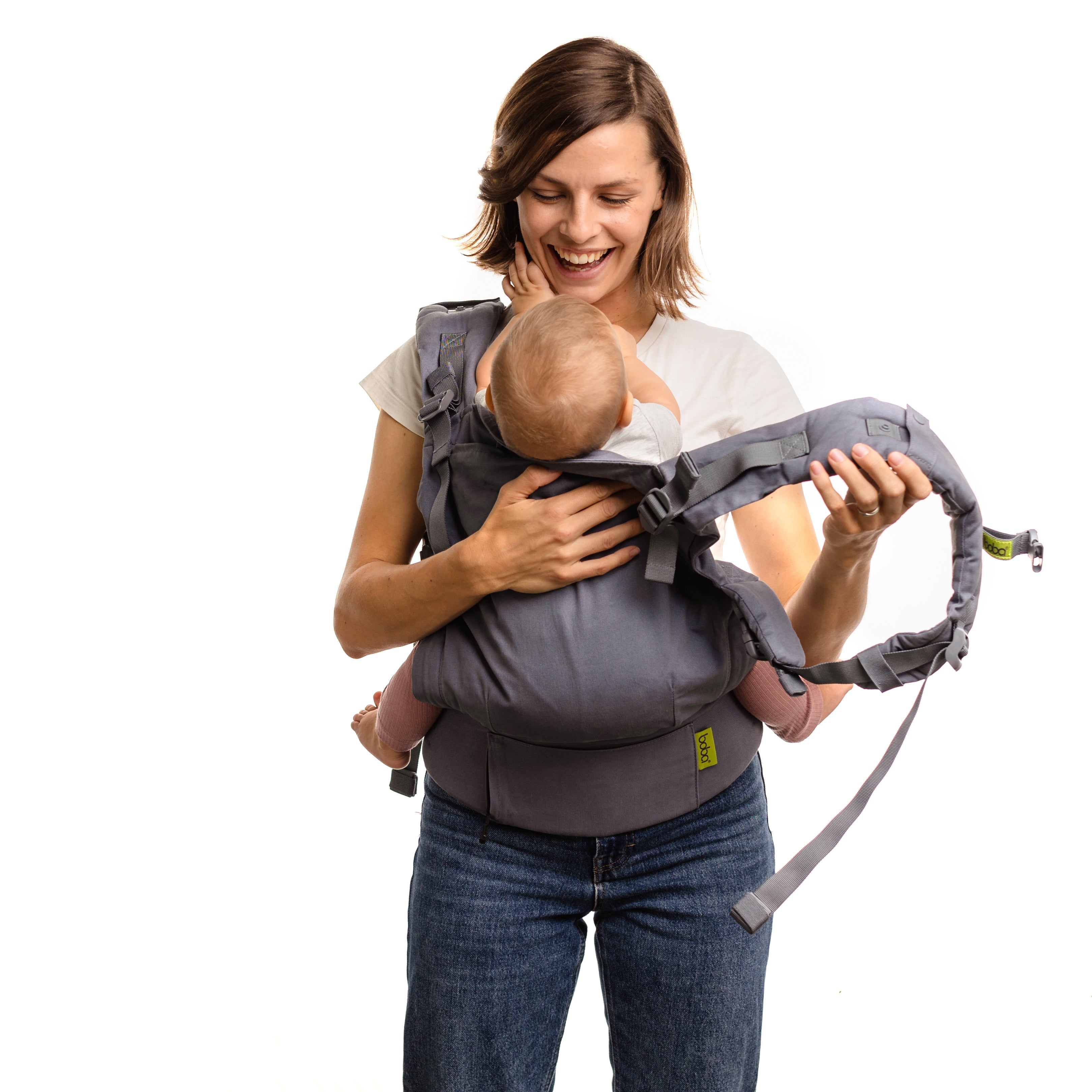 Happy young confident new mom is putting on the boba x gray carrier. She will wear her baby girl in the ergonomic front carry.