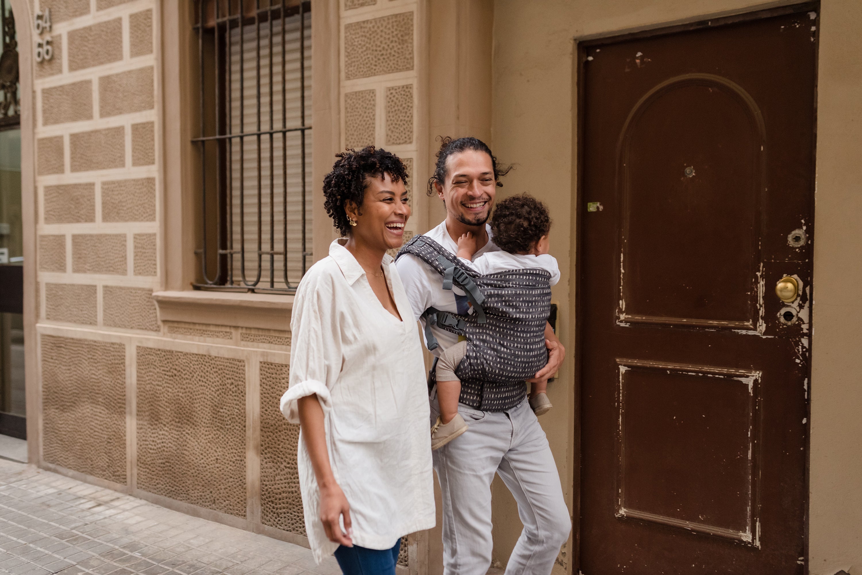 A happy mixed race couple walking on the street with their toddler girl in the boba x denim rain carrier.